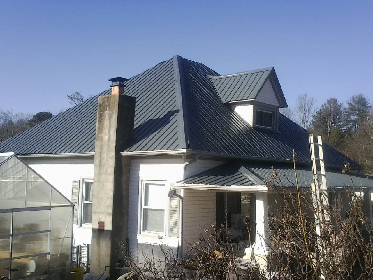 Dark blue standing seam metal roof on a white farmhouse with dormer — Slate & Tile Roof Repair by Roofing Brothers in Stilesville