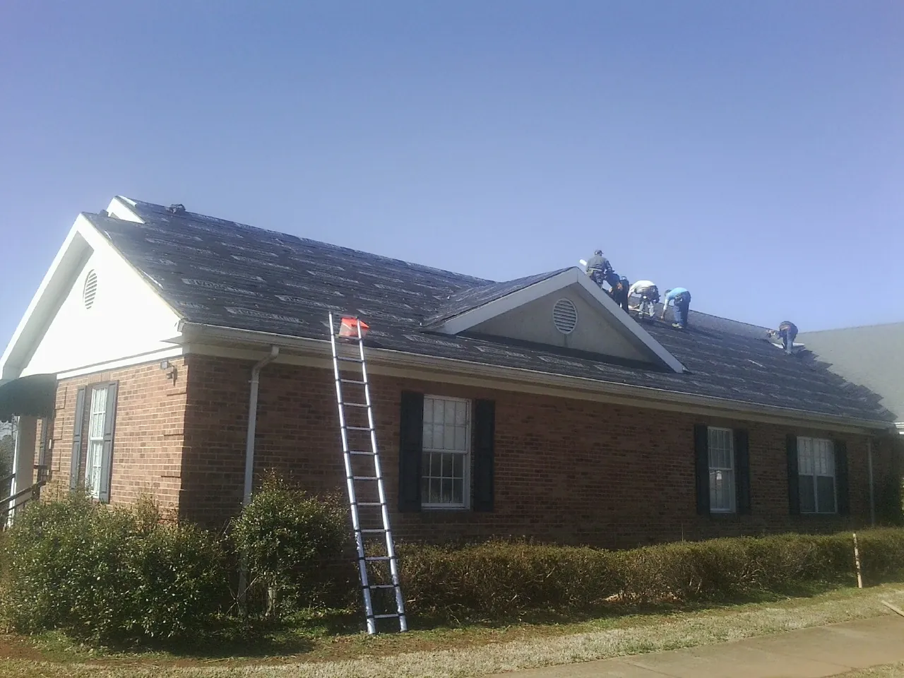 Crew tearing shingles off a brick ranch roof with a ladder set — Emergency Roof Repair work by our crew in Stilesville