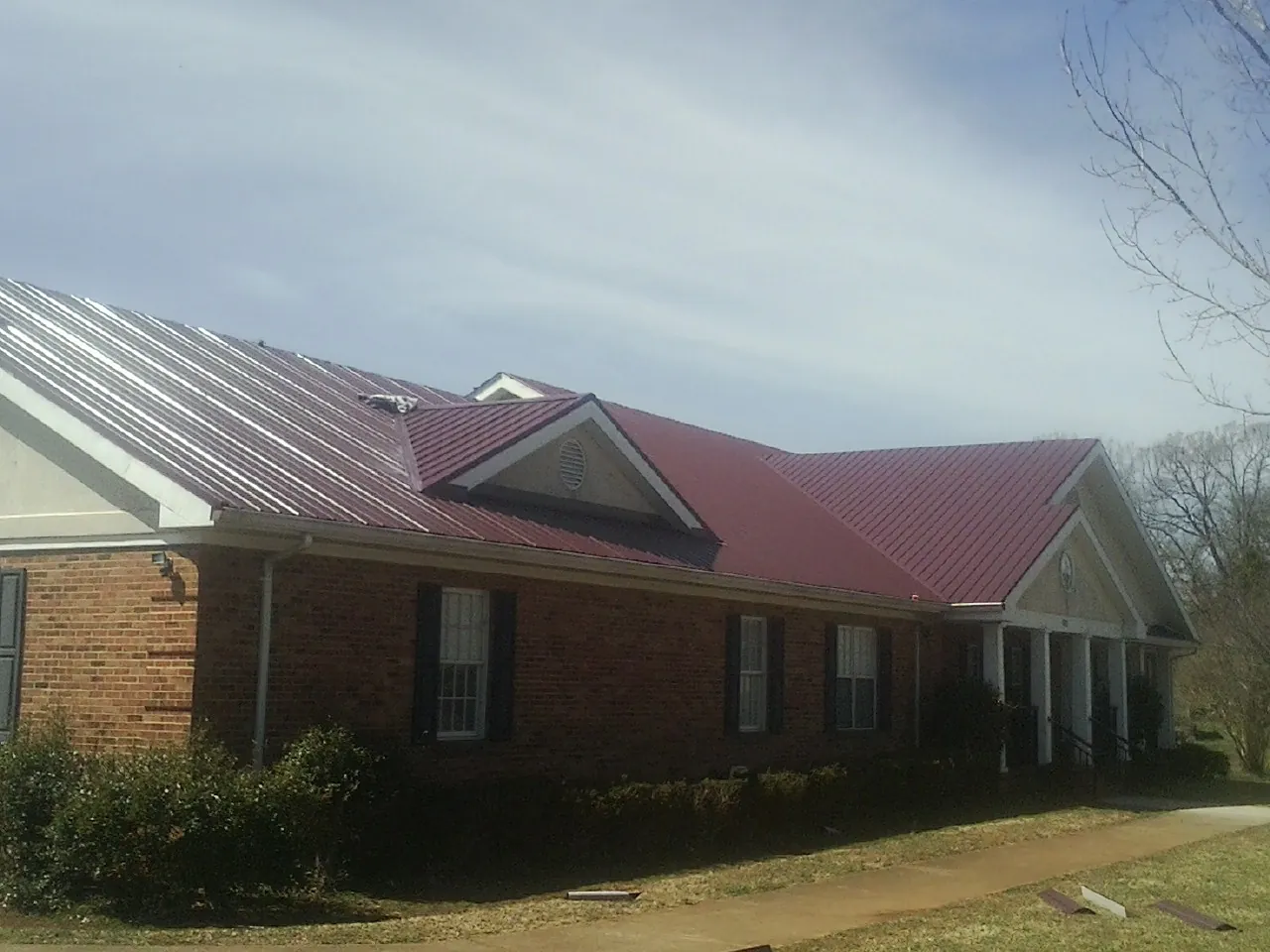 Red metal roof with gabled entries on a long brick building, from a Hail Damage Roof Repair job in Stilesville