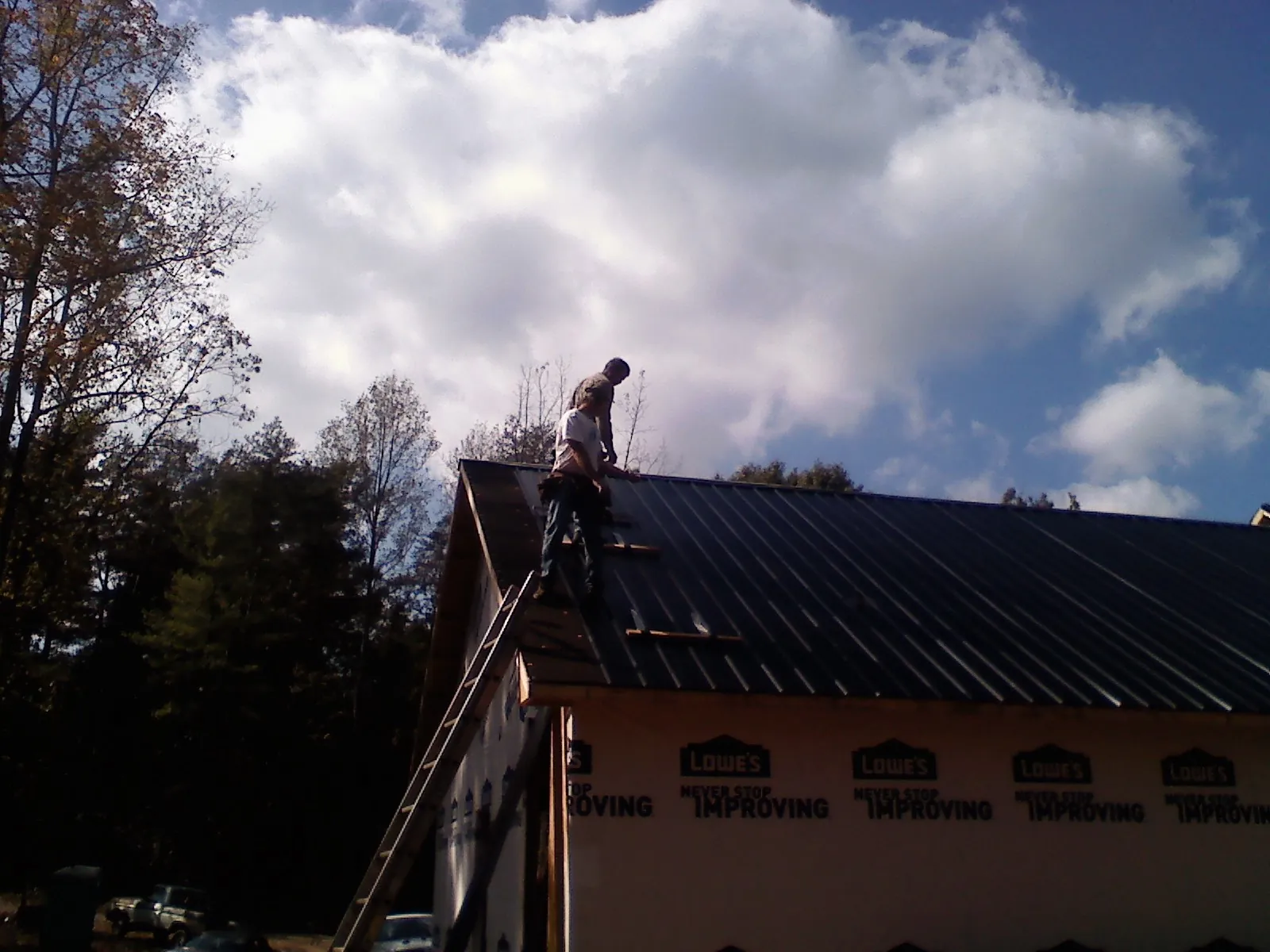 Roofer fastening dark metal panels high against a cloudy sky, from a Roof Inspection job in Stilesville