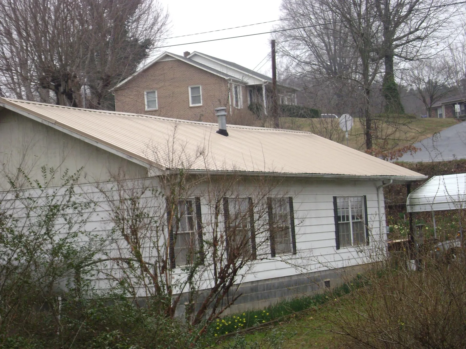 Tan metal roof on a white sided house set into a hillside — Commercial Roofing by Roofing Brothers in Stilesville